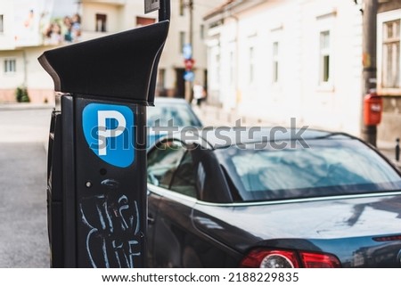 Parking meter with solar panel to get parking ticket on a narrow street in Europe next to a modern car
