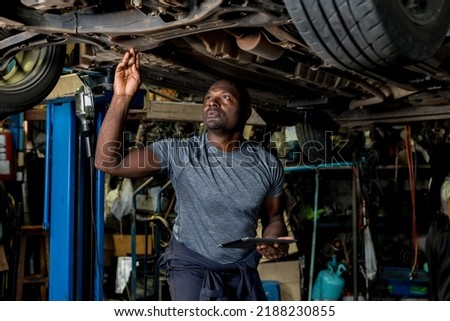 Professional Car Mechanic is Investigating Under a Vehicle on a Lift in Service. Auto Service Worker Checking Car Under Carriage Look For Issues. Car service technician check and repair customer car. Royalty-Free Stock Photo #2188230855