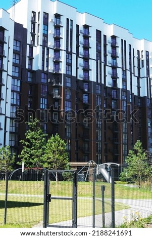 Modern residential complex, next to which there is a playground and a walking area with trees and grass. Vertical photo