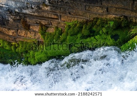 The fast moving water, layer of green moss and a stone wall makes an energetic eye catching nature photograph.