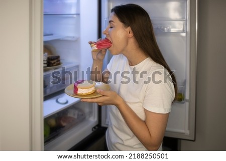 Woman eats a sweet delicious calorie sandwich with cream in her pajamas at night near the refrigerator. Concept: night meal, calories, food during stress and depression, bulimia, eating disorder Royalty-Free Stock Photo #2188250501