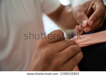 Male tailor using needle for making pink dress