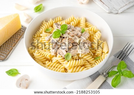 Fusilli pasta with mushrooms, cheese and fresh basil in a plate on a white wooden background