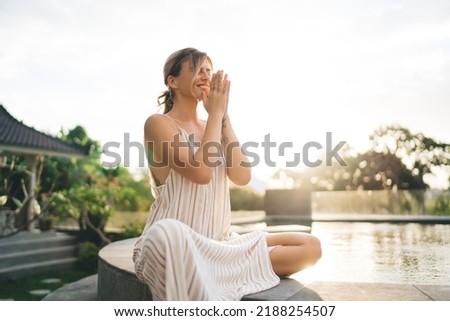 Young pleased woman practicing yoga and meditating on swimming pool edge in yard of resort hotel. Tourism, vacation and weekend. European girl. Sunset. Idyllic and tranquility lifestyle on Bali island Royalty-Free Stock Photo #2188254507