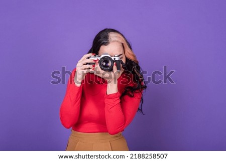 Attractive young lady taking a photo with her film camera over a violet background.  Studio shot.