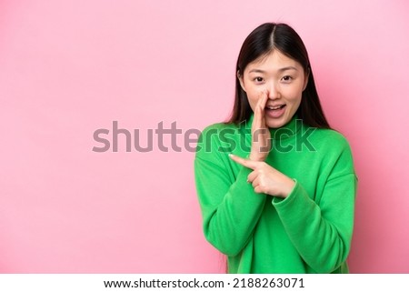 Young Chinese woman isolated on pink background pointing to the side to present a product and whispering something Royalty-Free Stock Photo #2188263071