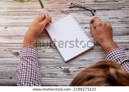 Man writing in notepad mock up, using his left hand. Conceptual photo of lefthanded day. Copy space