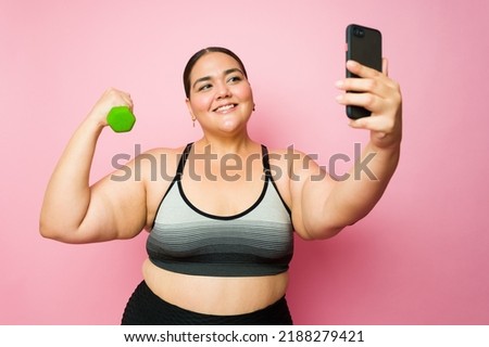 Beautiful fat young woman taking a selfie lifting dumbbell weights with her smartphone while doing her fitness workout