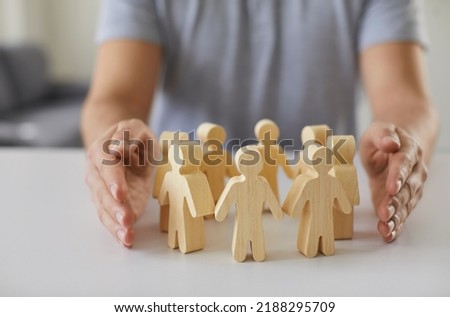 Social protection. Wooden figurines of people surrounded by man's hands symbolizing care for employees, customers or family. Close-up of figurines of people standing in circle on table and male Royalty-Free Stock Photo #2188295709