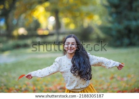Portrait of a little beautiful girl of 9 years old with long dark hair in bright clothes. Happy child in autumn park. Fall.
