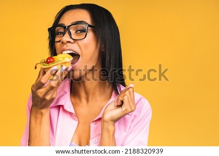 Black american african happy woman eating cake dessert isolated over yellow background. Eating cupcake. Diet unhealthy food concept.
