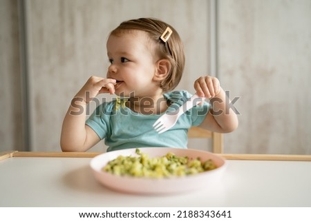 one girl small caucasian child toddler sitting at the table at home eating food alone using plastic fork childhood growing up and development concept copy space healthy eating bright photo