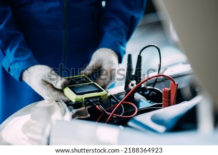 close up view of automotive mechanics repairman using a digital battery tester to check and analyze the battery in the car, check the mileage of the car, auto maintenance service concept. Royalty-Free Stock Photo #2188364923