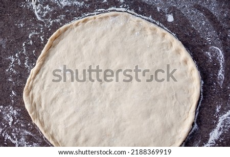 Rolled out pizza dough on floured slate surface, photographed overhead with natural light
