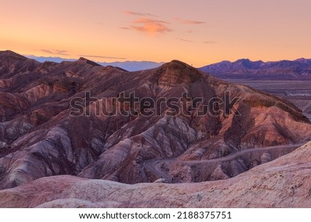 Hiker climbing hilly badlands at sunset; Zabriskie Point, Death Valley National Park, California