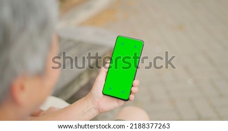 rear view of gray hair old senior asia man looking green screen phon in hand sitting on bench outdoor