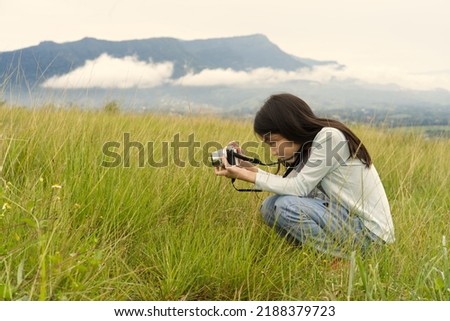 An Asian kid who is sitting and taking picture from her digital camera with mountain and clouds in background from Thailand.
