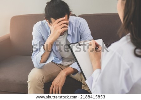 Asian young man, male has mental symptoms which must have been therapy and stress, sitting on couch to consult to psychologist during the session taking notes to find out how to treat the therapist. Royalty-Free Stock Photo #2188415853