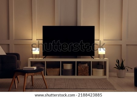 Modern TV on cabinet, armchair and lamps indoors. Interior design Royalty-Free Stock Photo #2188423885