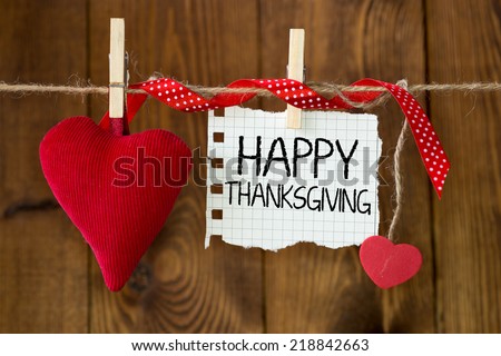 Happy thanksgiving message written on a paper hanging on the clothesline on wooden background with two hearts