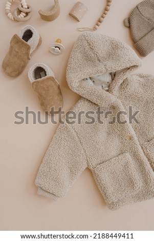 Warm winter children's jacket, suede booties, hat, pacifier, toys. Baby clothes and accessories set on neutral beige background. Fashion Scandinavian children's clothes. Flat lay, top view.