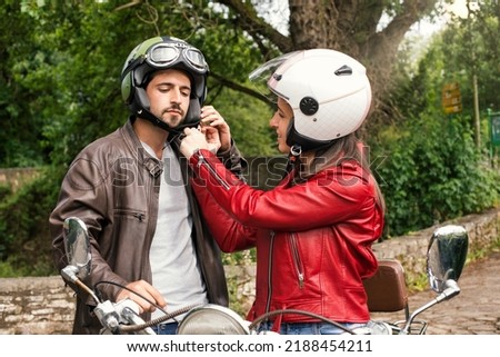 woman putting on and securing the helmet to the man. She couple on scooter putting on helmets. young couple looking out for road safety tightening helmet straps before traveling. Rider front Royalty-Free Stock Photo #2188454211