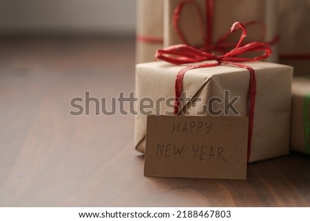 Brown paper gift boxes with red bow and Happy New Year paper card on walnut table with copy space, shallow focus