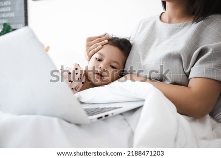 Mom and little daughter using laptop at home in summer holiday, Child looking at computer screen, Watching movies Or cartoon videos for kids on bed.