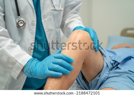 Doctor check Asian senior or elderly woman patient scar surgical total knee joint replacement Suture wound surgery arthroplasty on bed in nursing hospital ward, healthy strong medical concept. Royalty-Free Stock Photo #2188472101
