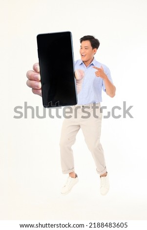 Full length body portrait of an energy young handsome Asian man, in office casual wear, hold big smart phone to show the app screen on white isolated background.