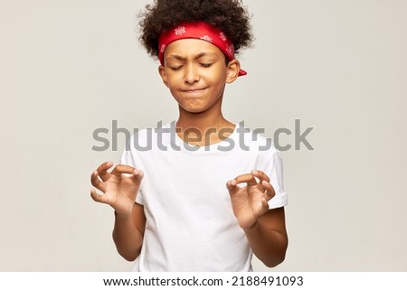 African american boy kid in red bandana and white mockup shirt doing yoga practice, trying to meditate keeping fingers in mudra sign, doing stress relief techniques on gray background