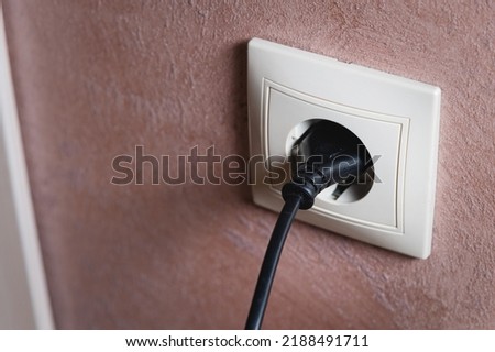 Electric socket on a pink wall. The black wire plug is connected. Renovated backdrop of studio apartment. Blank copy space single white plastic socket