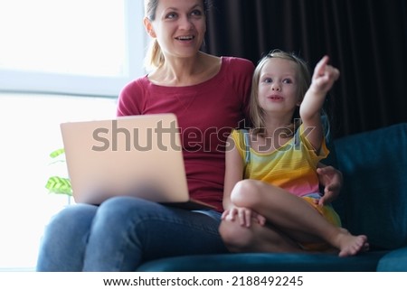 Portrait of mother and child sitting on sofa with laptop looking away in surprise
