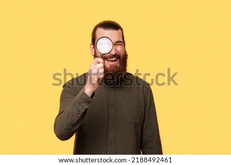 A photo of a young bearded man searching with a magnifying glass