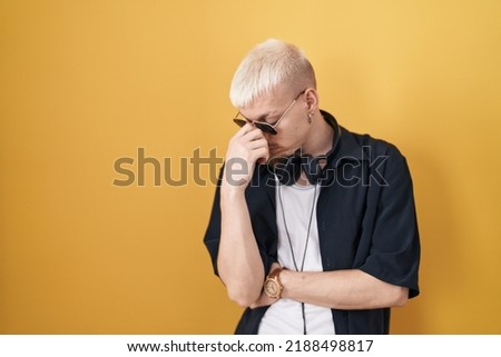 Young caucasian man wearing sunglasses standing over yellow background tired rubbing nose and eyes feeling fatigue and headache. stress and frustration concept. 