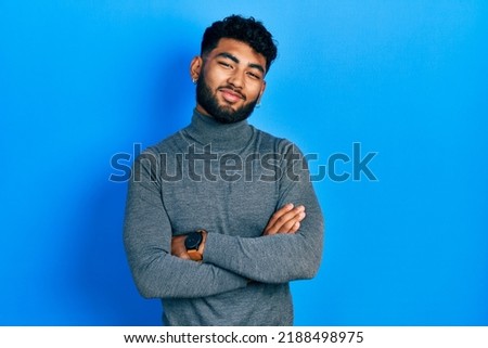 Arab man with beard wearing turtleneck sweater happy face smiling with crossed arms looking at the camera. positive person. 