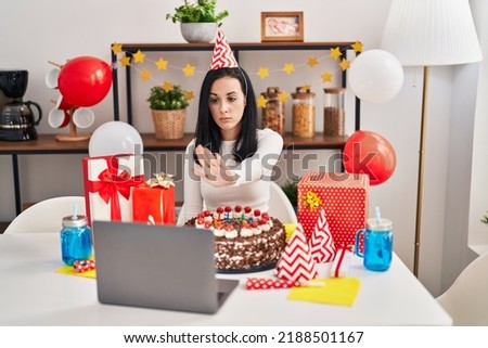 Hispanic woman celebrating birthday with big chocolate cake doing video call with open hand doing stop sign with serious and confident expression, defense gesture 
