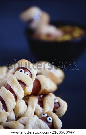 Fun food for kids. Mummy hot dogs (or pigs in a blanket) on a blue rustic table with a bowl of ketchup and mustard dip, with spider web design. Selective focus with blurred foreground and background.
