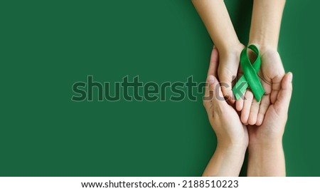 Adult and child hands holds green ribbon on green background. World lymphoma awareness day. September 15. Liver, Gallbladders bile duct, kidney Cancer and Lymphoma Awareness month. Banner. copy space Royalty-Free Stock Photo #2188510223