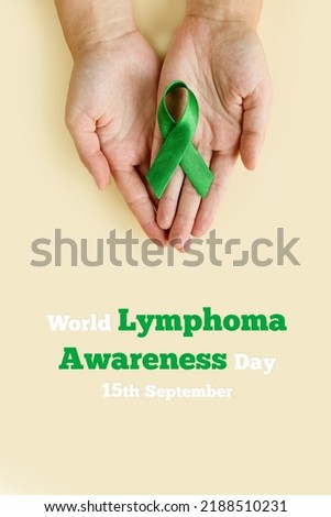 Adult hands holds green ribbon on beige background. World lymphoma awareness day. September 15. Liver, Gallbladders bile duct, kidney Cancer and Lymphoma Awareness month. Vertically photo Royalty-Free Stock Photo #2188510231