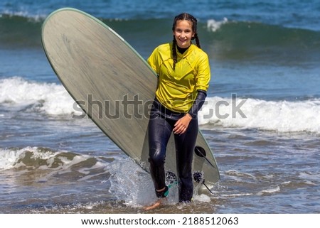 Young caucasian woman coming out of the sea water with a surfboard