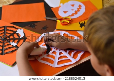 Close-up of children's hands that create paper crafts for Halloween. Homemade decorations for the holiday. Hobbies, what to do with children. Selective focus.