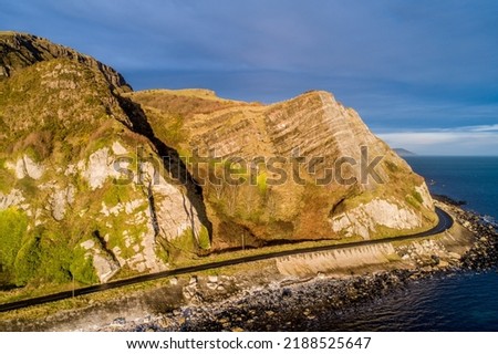 Northern Ireland, UK. Atlantic coast. Cliffs and Antrim Coast Road, a.k.a. Causeway Costal Route. One of the most scenic coastal roads in Europe. Aerial view near Garron Point in sunrise light Royalty-Free Stock Photo #2188525647