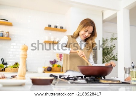 Young beautiful Asian woman enjoy cooking healthy food and pasta in cooking pan on stove in the kitchen at home. Happy female having dinner meeting party celebration with friends on holiday vacation. Royalty-Free Stock Photo #2188528417