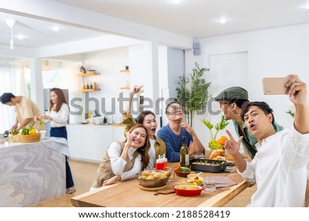 Group of Cheerful Asian man and woman friends enjoy dinner party using mobile phone taking selfie together at home. Happy male and female reunion meeting and celebrating on holiday event vacation.