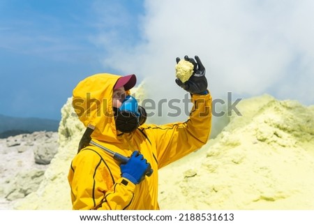 woman volcanologist on the background of a smoking fumarole examines a sample of a sulfur mineral