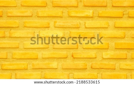 Brick wall painted with yellow paint pastel bright tone texture background. Brickwork and stonework flooring interior with rock old pattern clean grid concrete uneven bricks design backdrop.