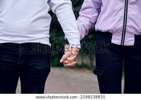 Young couple in love holding hands in the park. Close up picture of girlfriend and boyfriend, standing walking in the street. Romantic relationship in teenage time.