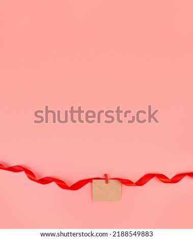 craft envelope attached to a swirling red ribbon isolated on a pastel pink background with copy space. Object for design to women's day, mother's day, anniversary, valentine day. Minimalism concept