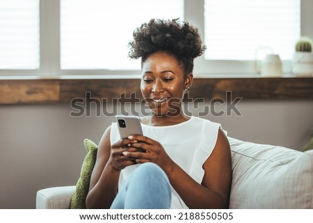 Cropped shot of an attractive young woman using her cellphone while sitting in the living room during the day. Keeping her social media fans updated Royalty-Free Stock Photo #2188550505